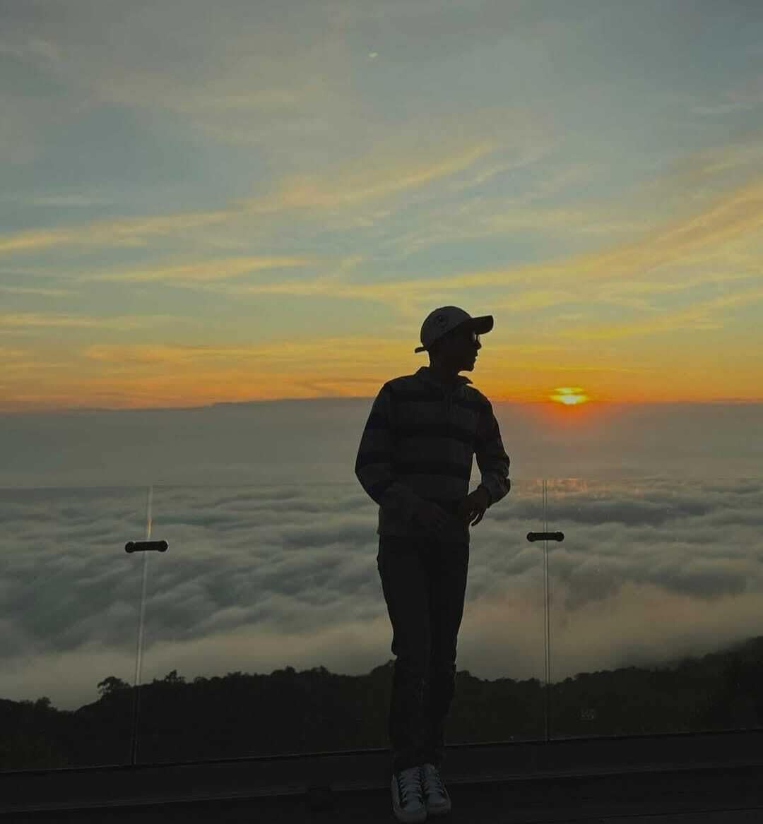 A person standing on a platform overlooking a sea of clouds at sunset.