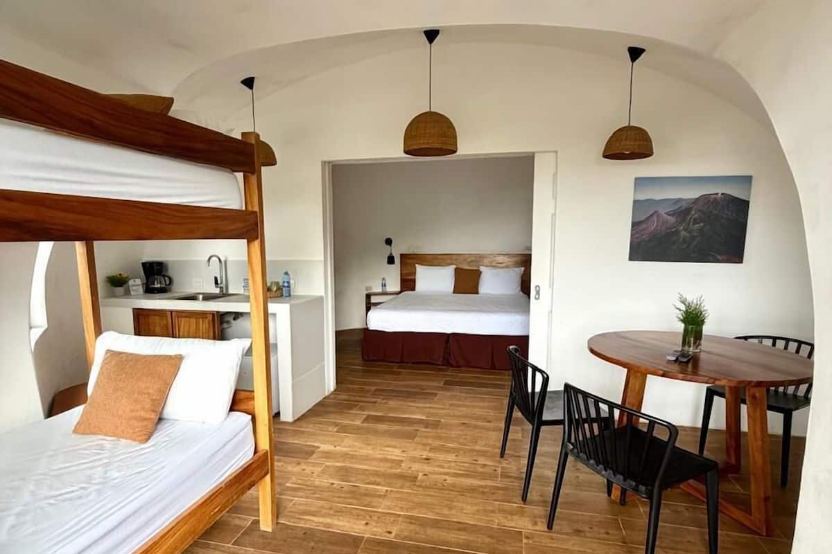 A room with a wooden bed, a dining table with chairs, and a kitchen area.