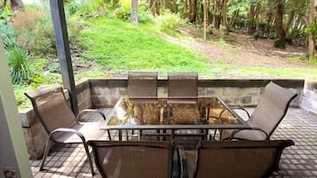 An outdoor patio with a glass-top table and wicker chairs, surrounded by a tiled floor and a metal roof.