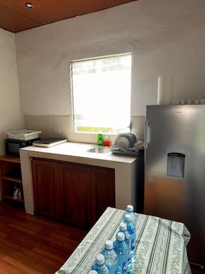 A compact kitchen with a window, a refrigerator, and a table with water bottles.