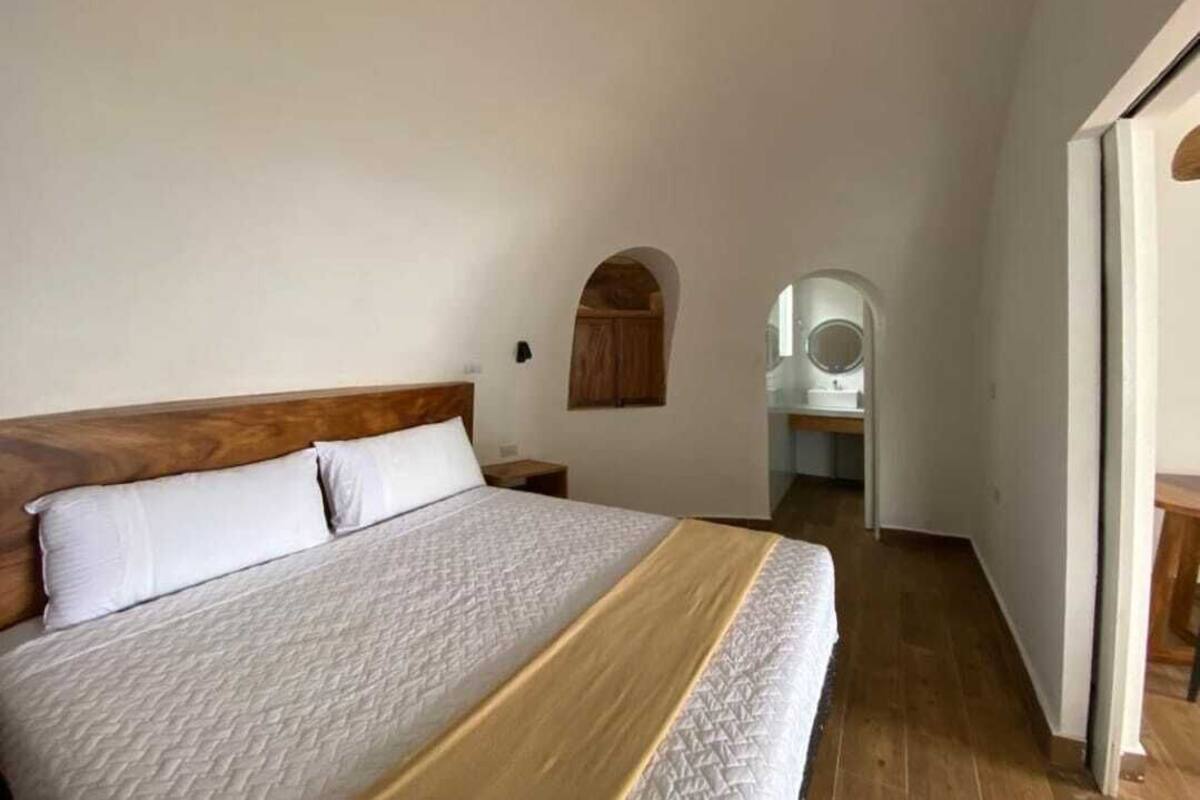 A bedroom with a wooden headboard, a bed with white bedding, a small wooden cabinet, and a white chair in the corner.