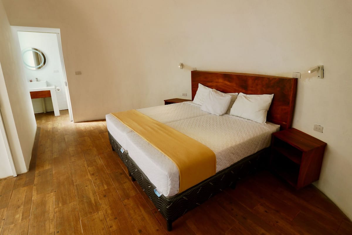 A double bed with a wooden headboard, two bedside tables, a bedside lamp, and a wooden floor.
