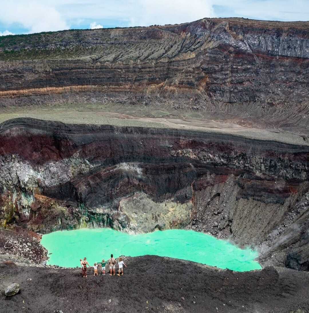 A large open pit with a turquoise pool at the bottom, surrounded by layered rock formations.