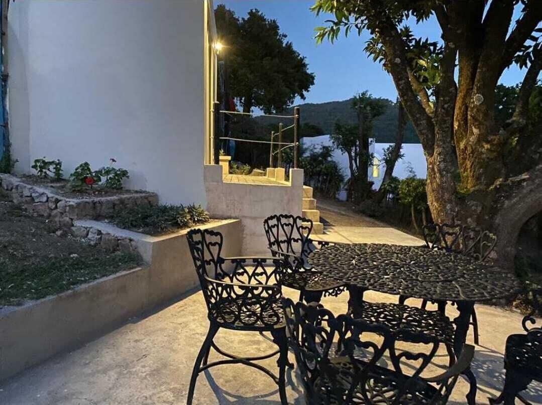 An outdoor seating area with a table and chairs, a stone staircase, and a view of a body of water and hills in the background.