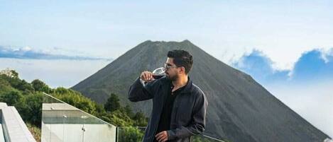 A person standing on a balcony overlooking a mountainous landscape with a glass railing.
