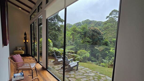 A spacious balcony with wicker furniture and a stone pathway leading to a seating area, overlooking a lush garden and forested hills. - Casa Mia Suite with Jacuzzi and Panoramic View (Monteverde)