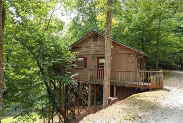 Situated on stilts in a forested area, this cabin offers a secluded retreat with a front porch and deck.
