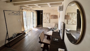 A modern room with a wooden floor, a desk with a chair, a hanging light fixture, and a large mirror.