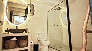 A modern bathroom with a glass shower enclosure, a round mirror, and a white sink with a vessel basin.