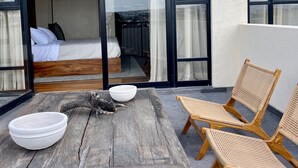 A modern room with a bed, a wooden table with a bowl, and wicker chairs.