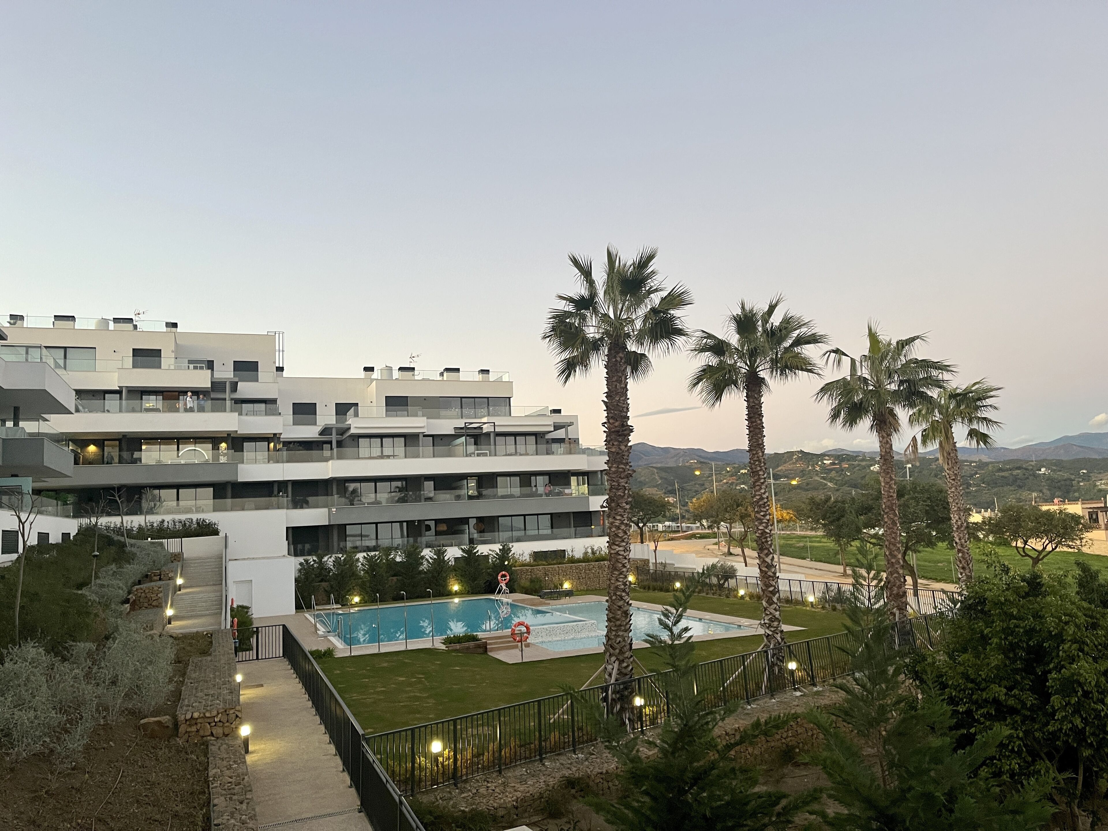 Un hotel moderno con varios pisos, una piscina y palmeras.