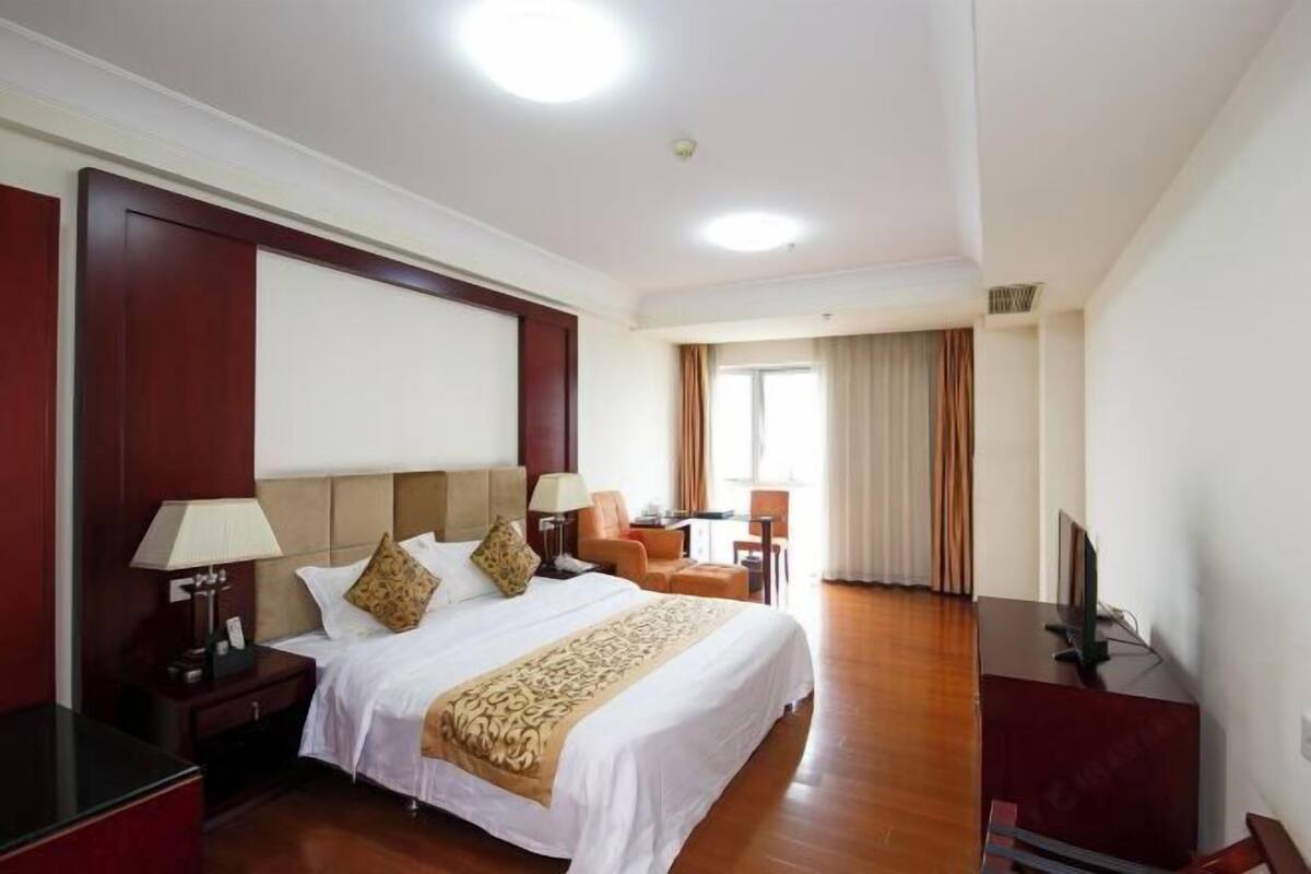 Ein Hotelzimmer mit einem großen Bett, zwei Nachttischen, einem Schreibtisch, einem Sessel und einem Fernseher.