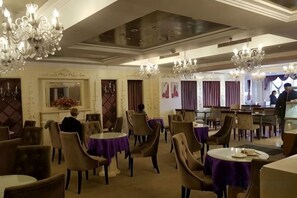 Ein Speisesaal eines Hotels mit runden Tischen, Stühlen und Kristalllüstern.