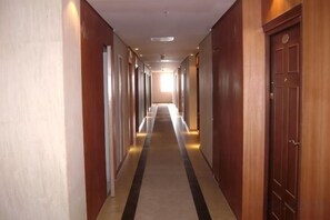 Un pasillo de hotel con puertas a ambos lados, suelo alfombrado y una lámpara en el techo.