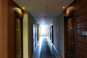 Ein Hotelgang mit Holztüren an beiden Seiten, einem Teppichboden und einer Lichtquelle am Ende des Ganges.