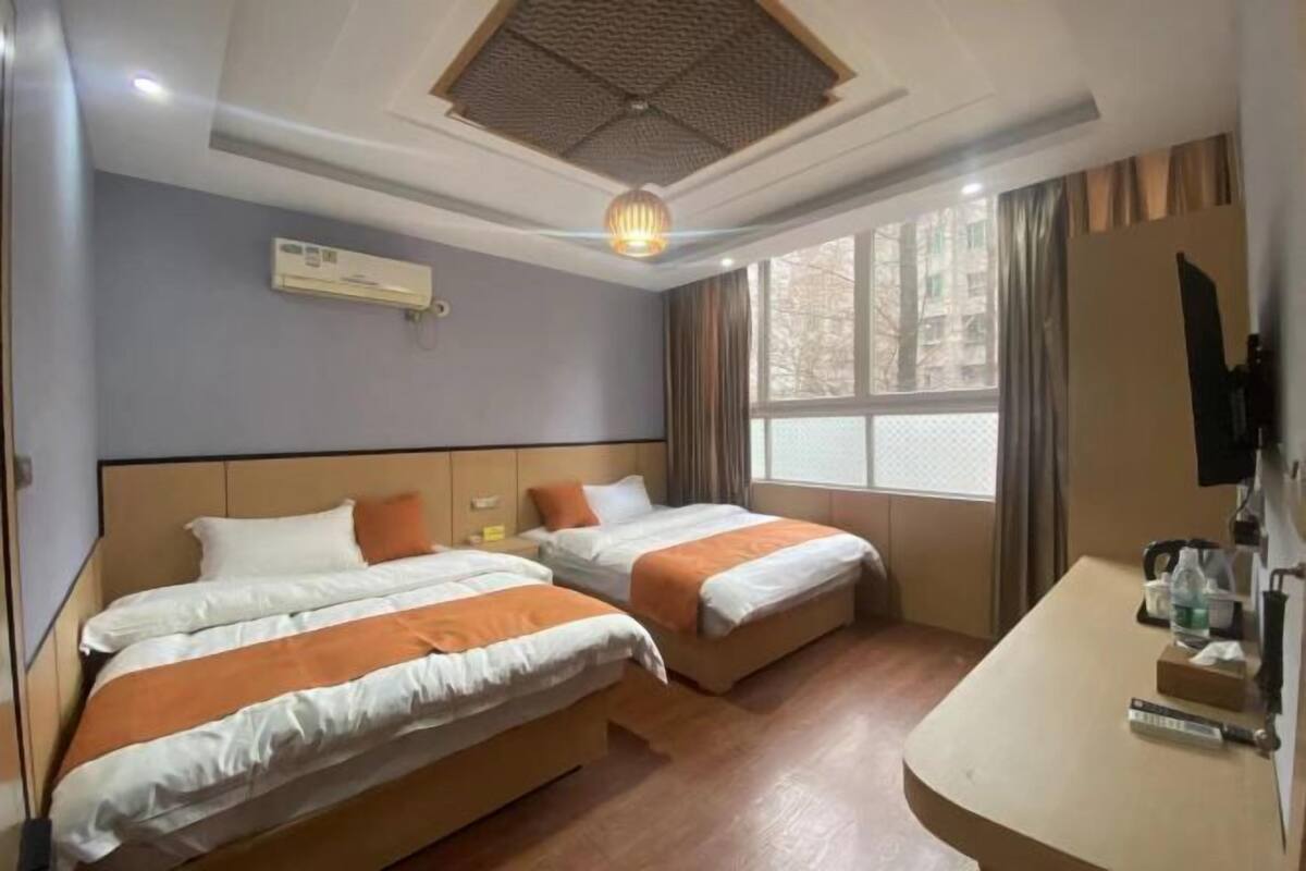 A hotel room with two beds, a desk, an air conditioning unit, and a window with curtains.