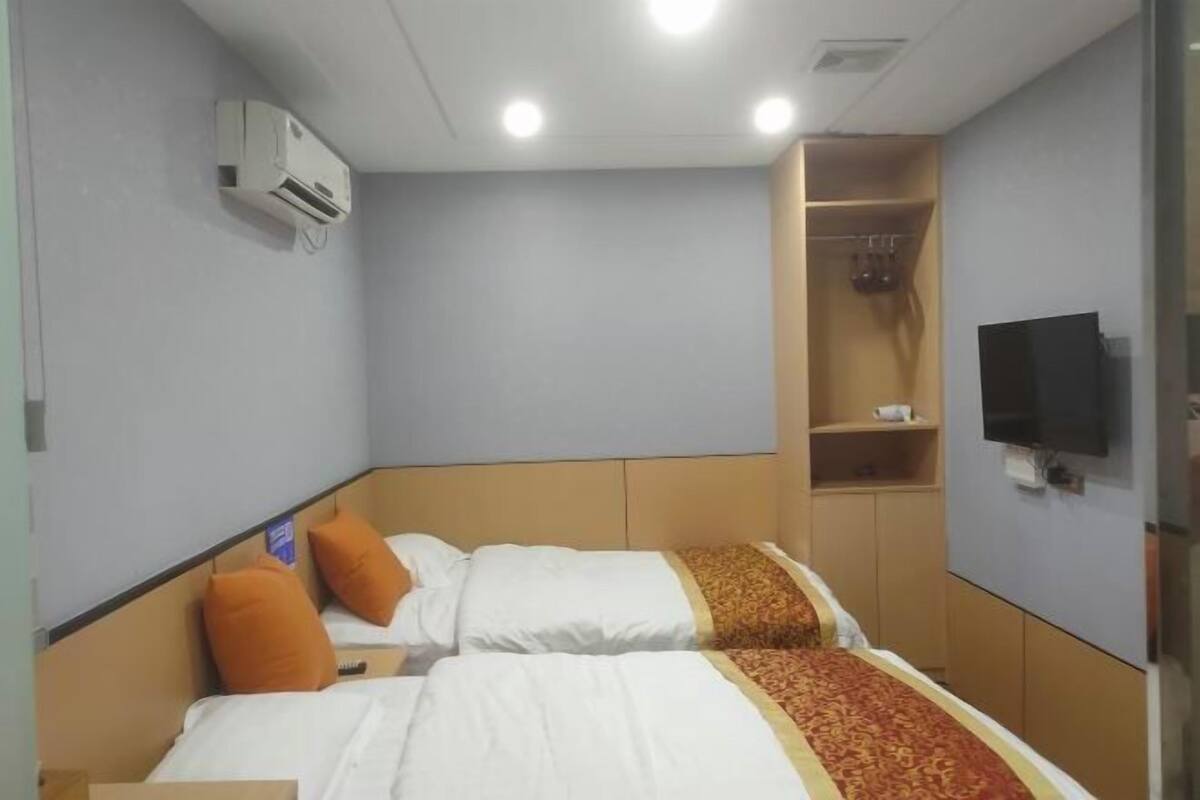 A hotel room with two beds, an air conditioning unit, a television, and a wardrobe.