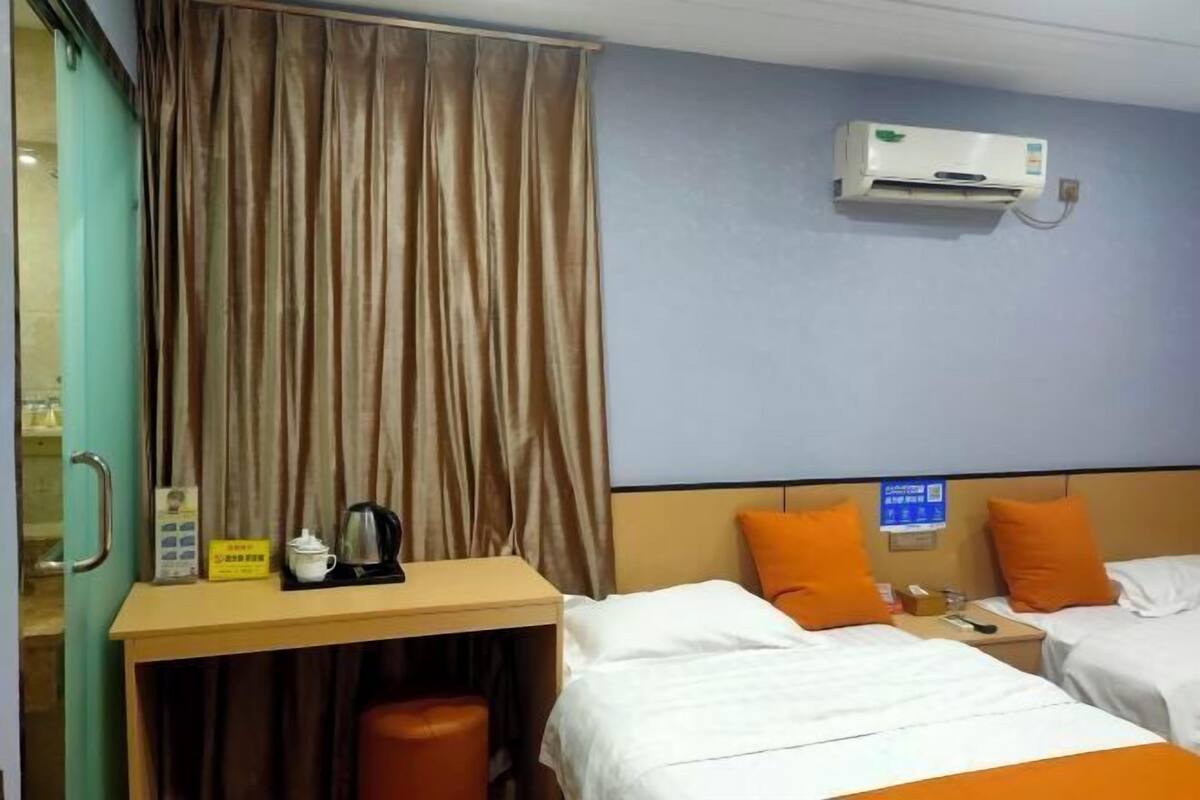 A hotel room with two beds, an air conditioner, a desk with a kettle, and a curtain.