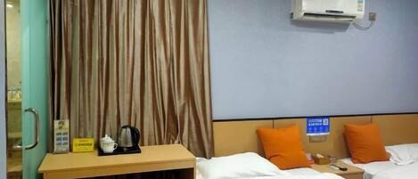 A hotel room with two beds, an air conditioner, a desk with a kettle, and a curtain.