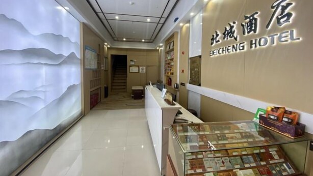 A hotel reception area with a modern design, a reception desk, and a display of various items. - Beicheng Hotel (Dazhu)