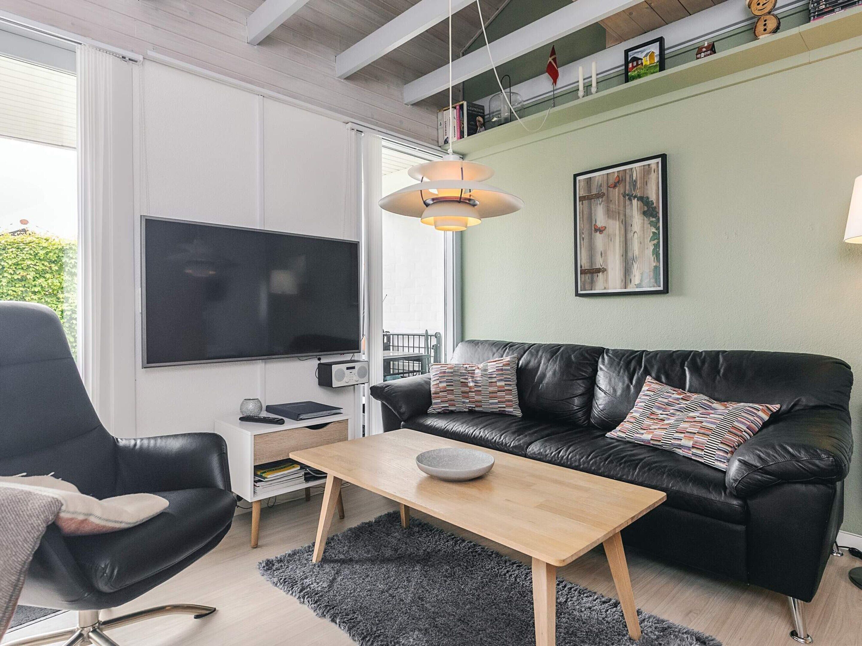 Una sala de estar moderna con un sofá de cuero negro, una mesa de centro de madera, un sillón negro, un televisor y un cuadro en la pared.