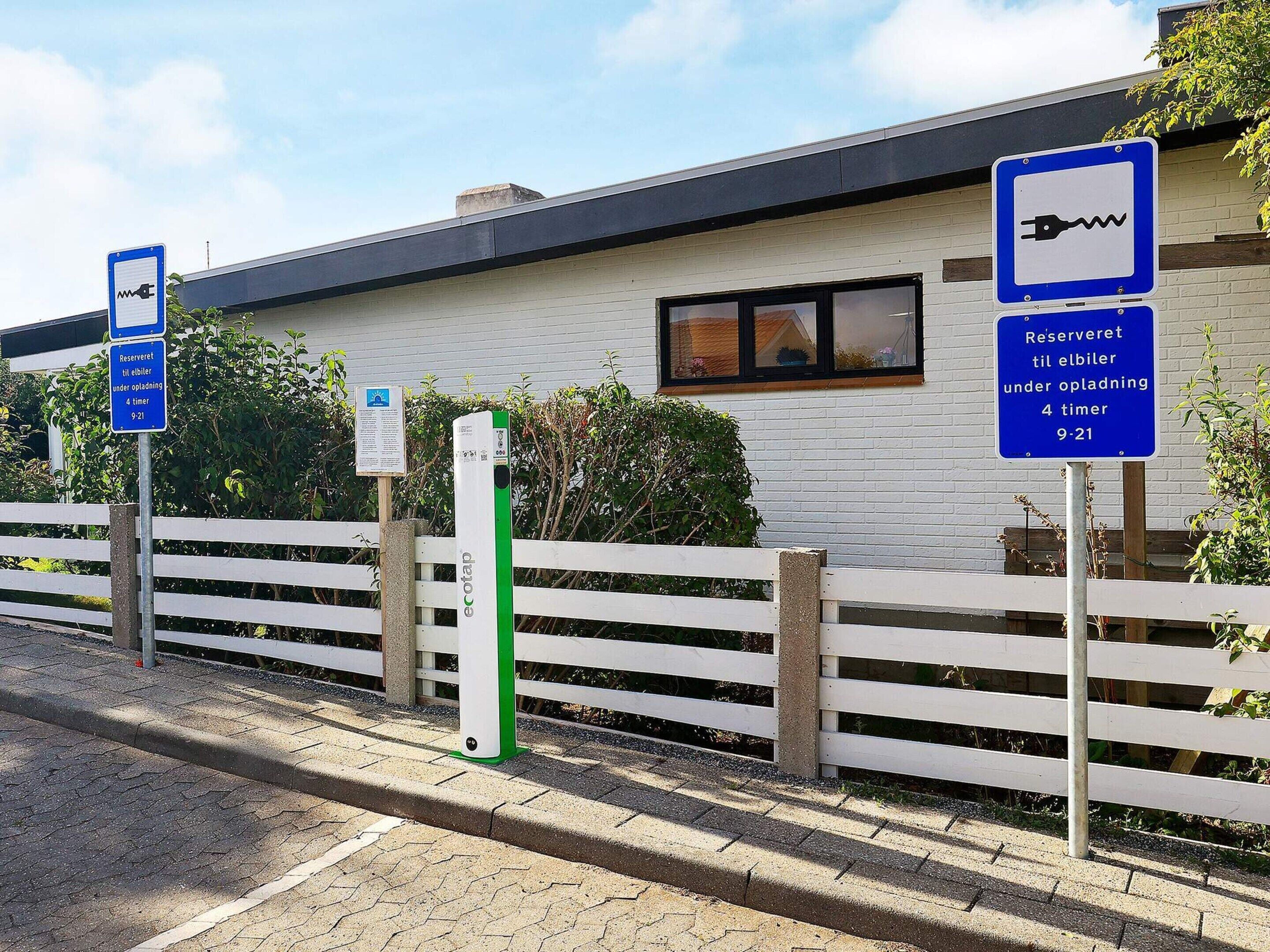 A building with a white facade, a wooden fence, and a parking area with electric vehicle charging stations.