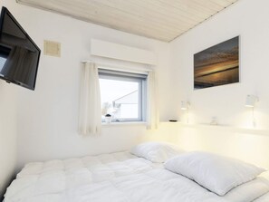 A bedroom with a bed, a window with curtains, a flat-screen TV mounted on the wall, and a painting above the bed. - 4 Person Holiday Home in Aeroskobing (Aeroskobing)