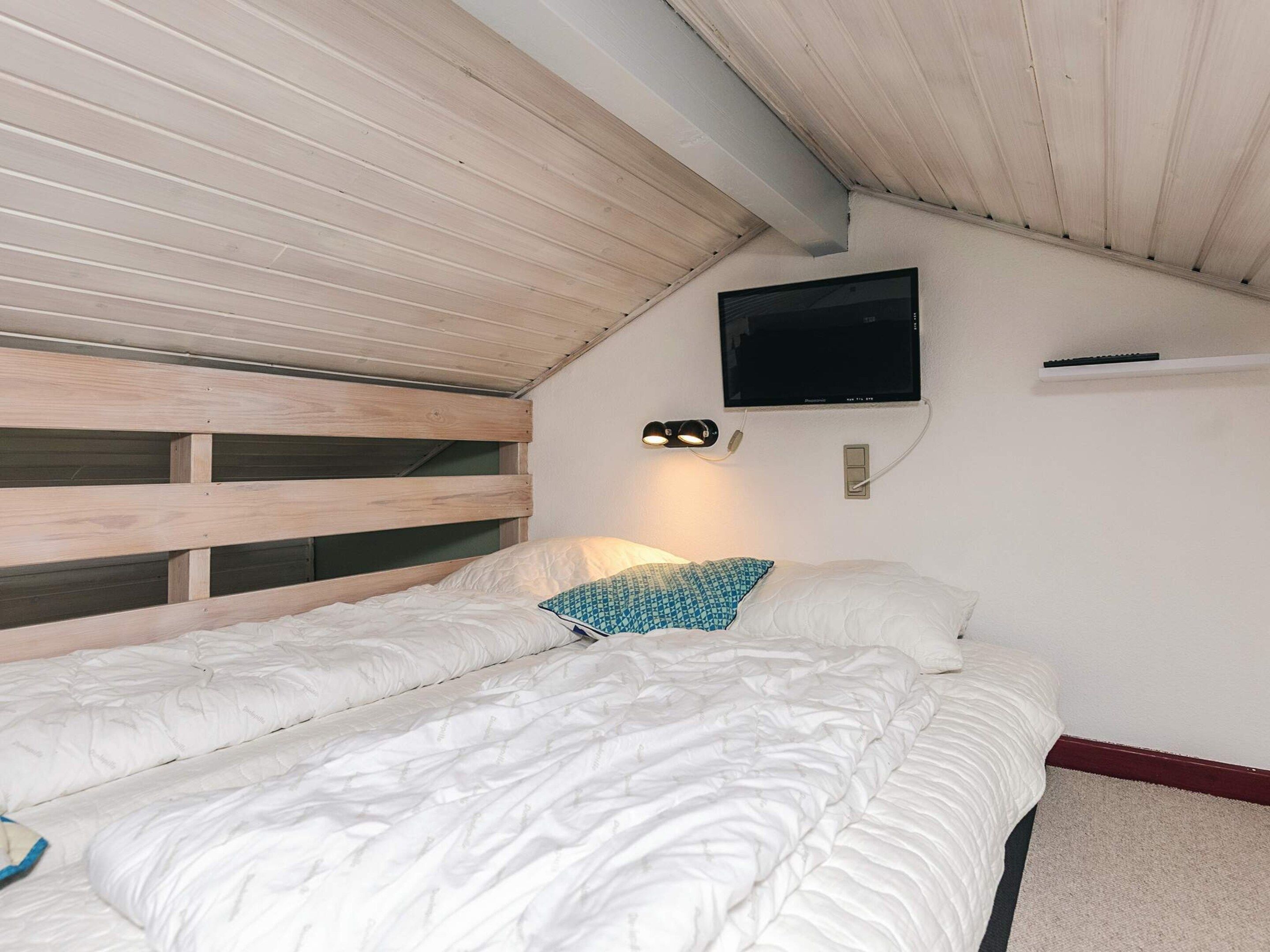 A bedroom with a bunk bed, a flat-screen TV mounted on the wall, and a bedside lamp.