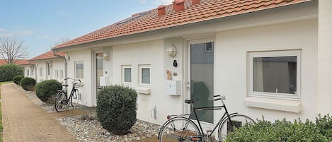 A row of white buildings with red-tiled roofs, bicycles parked outside, and a gravel pathway.
