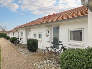 A row of white buildings with red-tiled roofs, bicycles parked outside, and a gravel pathway.