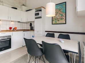Une cuisine moderne avec des meubles blancs, un four Bosch, un micro-ondes et un coin repas comprenant une table et des chaises.