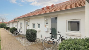 Fileira de edifícios brancos com telhados de telha vermelha, um caminho pavimentado e bicicletas estacionadas na frente.