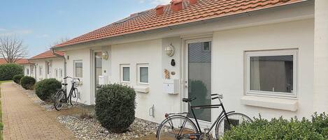 A row of white buildings with red-tiled roofs, a paved pathway, and bicycles parked in front.
