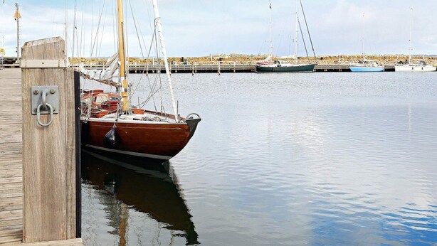 Een houten steiger met een vastgemaakt bootje, kalm water en een rotsachtige pier op de achtergrond.