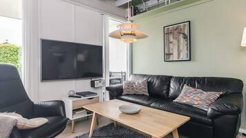 A modern living room with a black leather sofa, a wooden coffee table, a black armchair, a TV, and a painting on the wall.