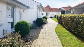 A pathway leading to a row of white houses with red roofs, surrounded by well-maintained hedges and a grassy area.