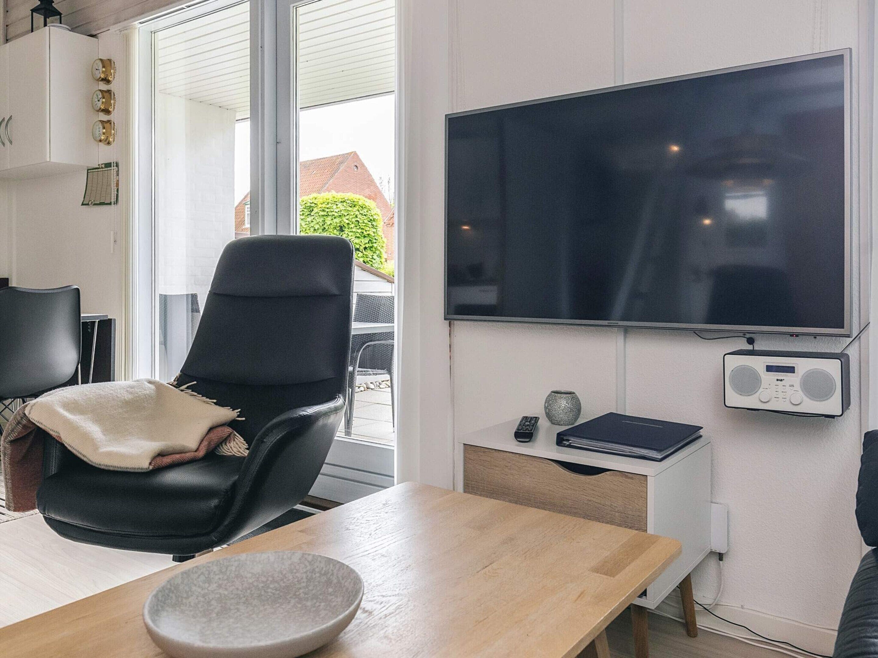 A modern living room with a large flat-screen TV, a black leather chair, a wooden table, and a small side table with a radio.