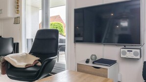Een moderne woonkamer met een grote flatscreen televisie, een zwarte leren fauteuil, een houten tafel en een klein bijzettafeltje met een radio.