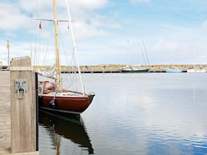 Un muelle de madera con un barco amarrado, una superficie acuática tranquila y una costa rocosa al fondo.