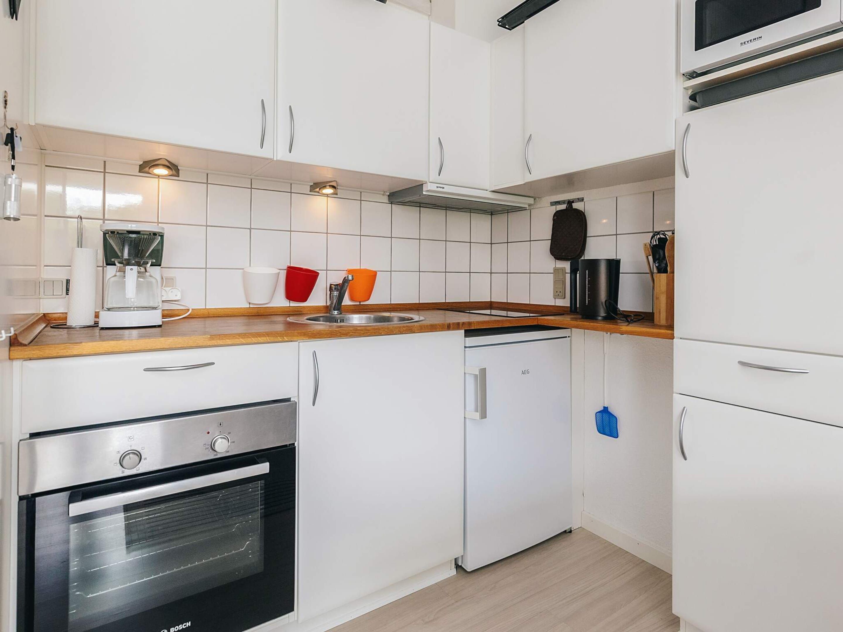 A compact kitchen with white cabinetry, a built-in oven, a coffee maker, and a microwave.