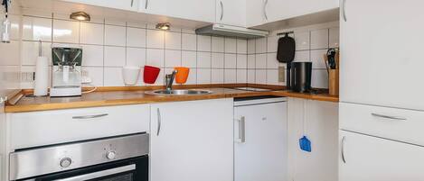 Une cuisine compacte avec des meubles blancs, un four encastré, une machine à café et un four à micro-ondes.