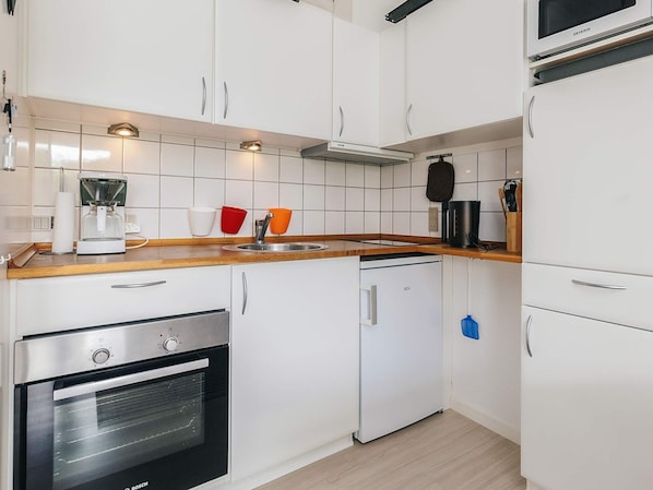 A compact kitchen with white cabinetry, a built-in oven, a coffee maker, and a microwave. - 4 Person Holiday Home in Aeroskobing (Aeroskobing)