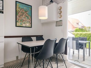 A dining area with a table and chairs, a hanging light fixture, a wall clock, and a framed map. - 4 Person Holiday Home in Aeroskobing (Aeroskobing)