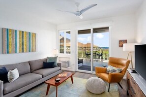 Relax in this stylish living room with a sofa, armchair, and flat-screen TV, leading to a patio with ocean views.