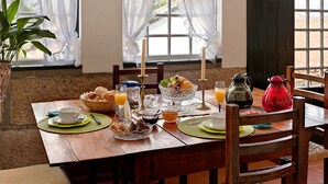 A wooden dining table set with breakfast items, including bread, fruit, and beverages, in a room with a view through a window.