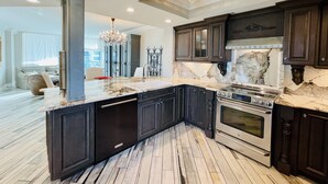 A modern kitchen with dark cabinetry, a marble countertop, and stainless steel appliances.