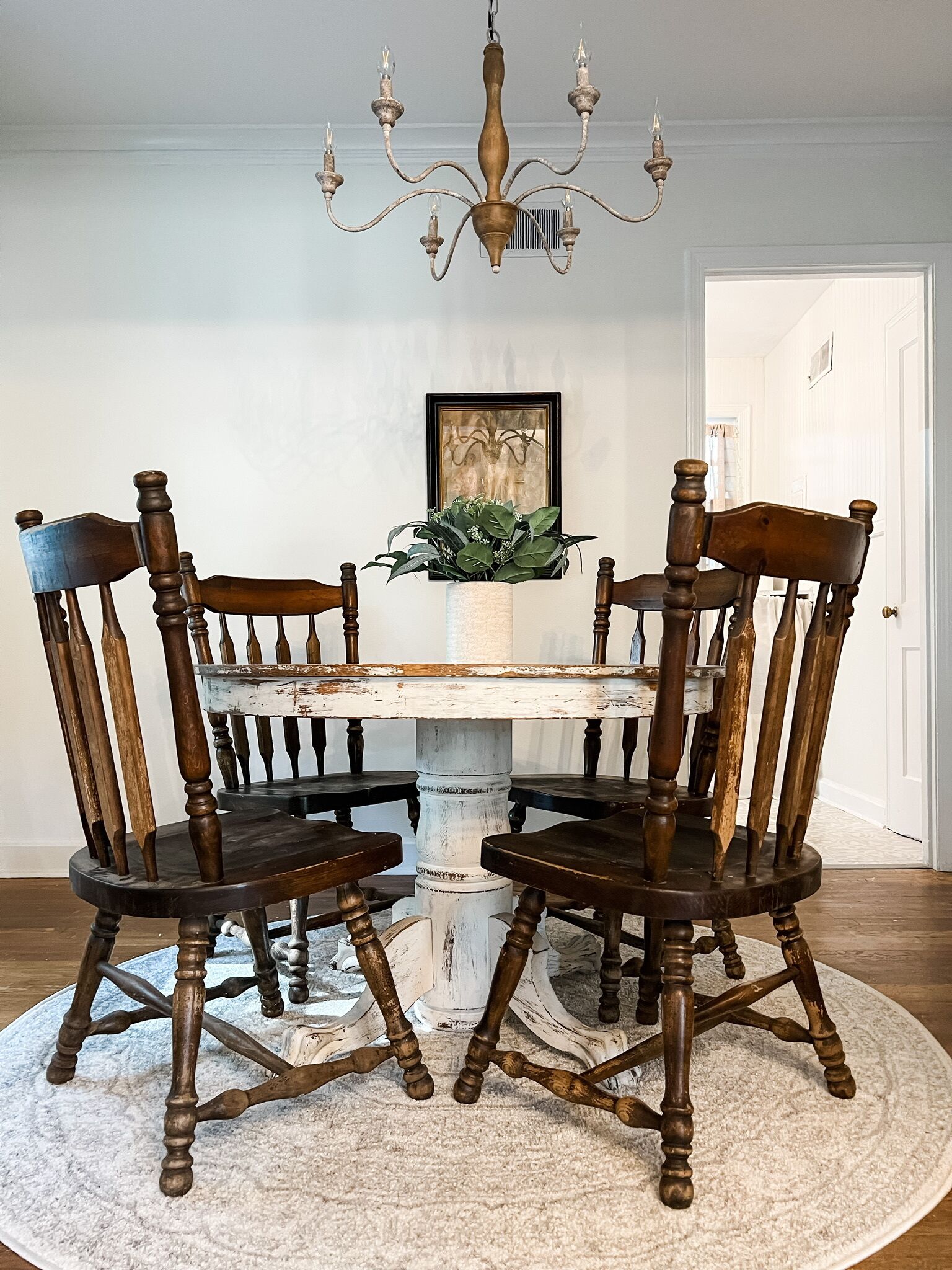 Une table à manger avec quatre chaises, un lustre, un tableau encadré et une plante posée sur un tapis.