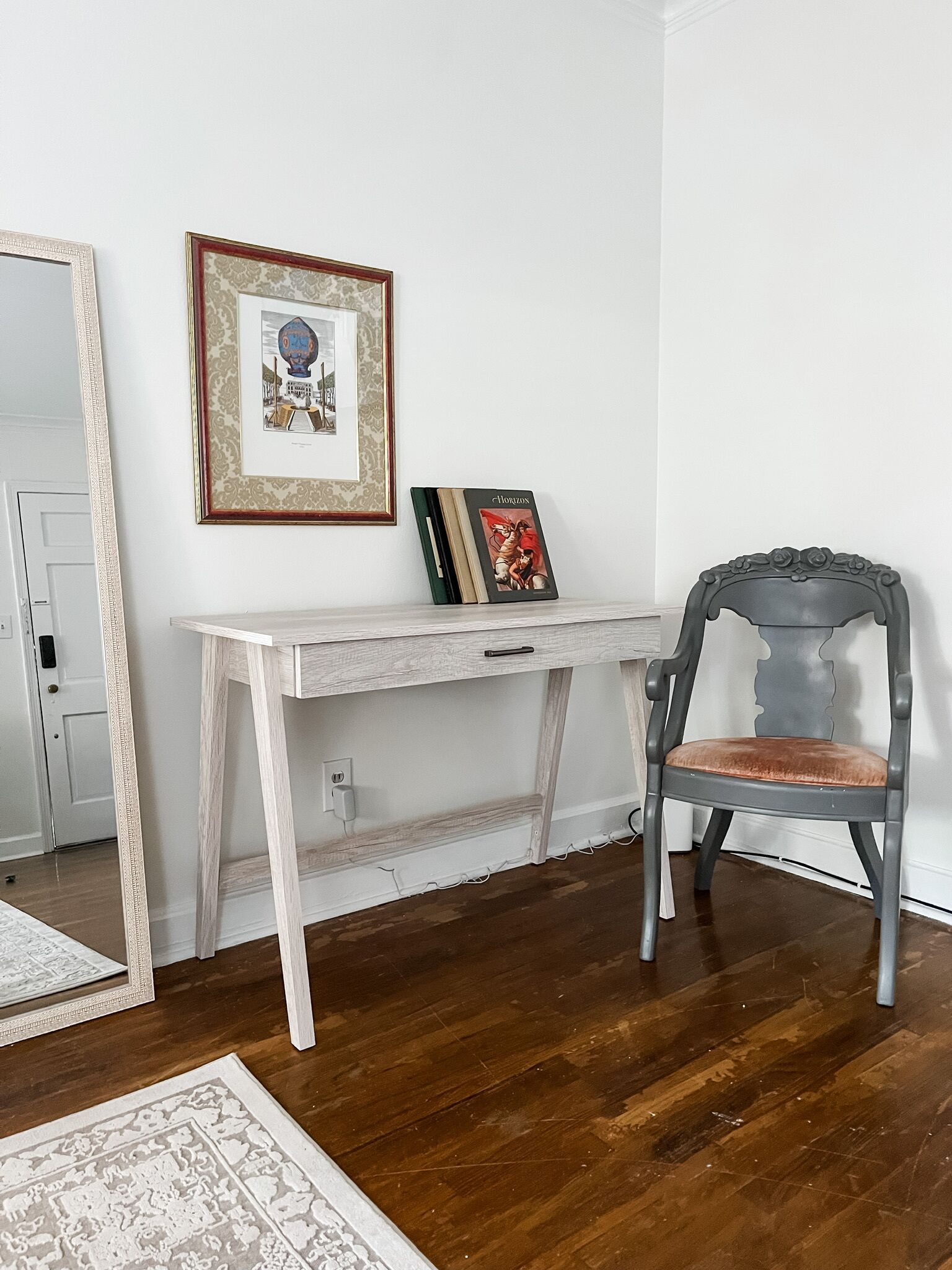 A room with a white desk, a framed picture, a book titled 'Horizon', and a vintage chair.