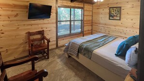 Een houten slaapkamer met een bed, een stoel, een televisie en een raam.