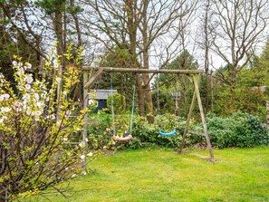 A garden with a wooden swing set, a small shed, and various shrubs. - 6 Person Holiday Home in Ulfborg (Ulfborg)